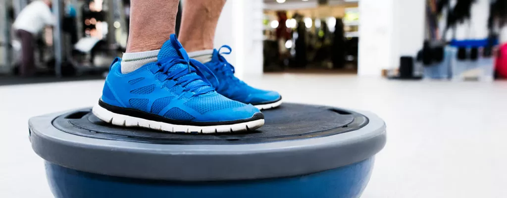 Male patient standing on balance board as part of vestibular therapy.